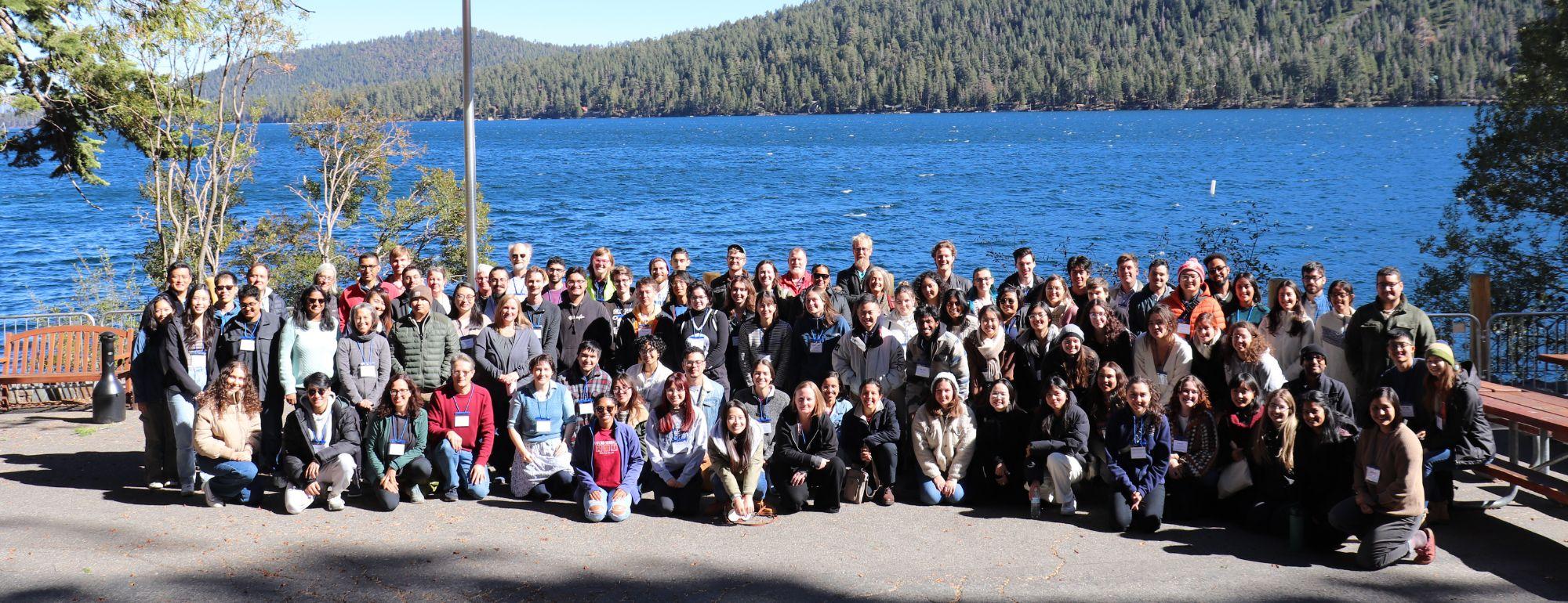 Group of individuals sitting and smiling at camera with lake and nature behind them.
